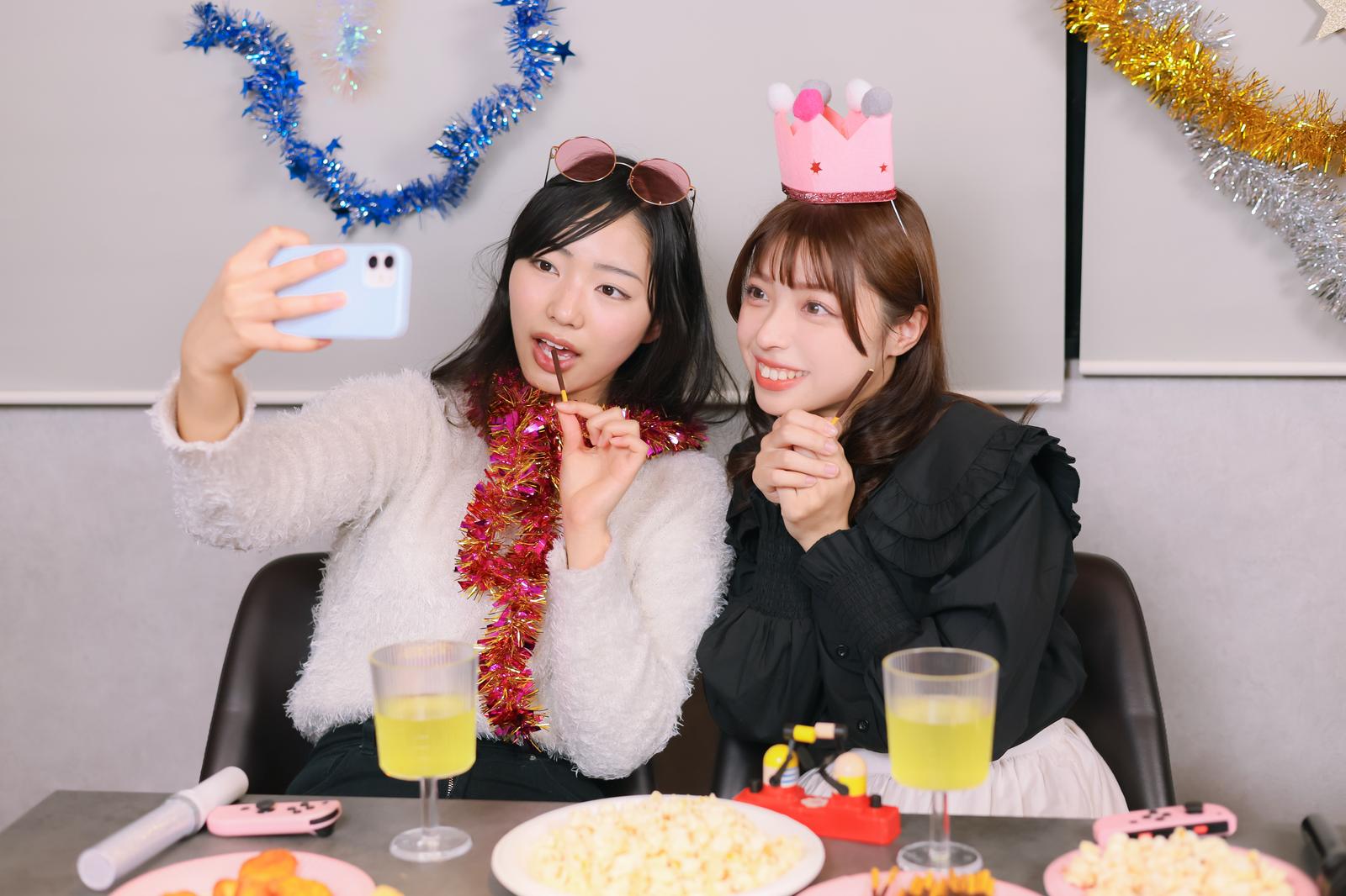 パーティー小物を装着した女性ふたりがスマートフォンで自撮りしている［モデル：なんこ 高尾実生］