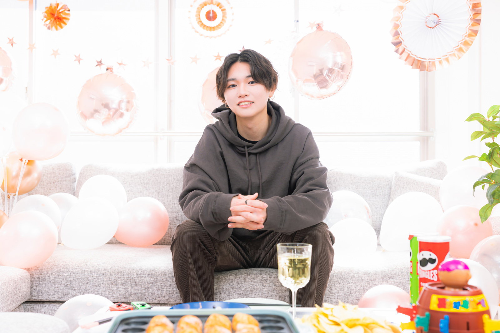 グレーのパーカーを着て座ってくつろいでいる男性［モデル：SHUN］