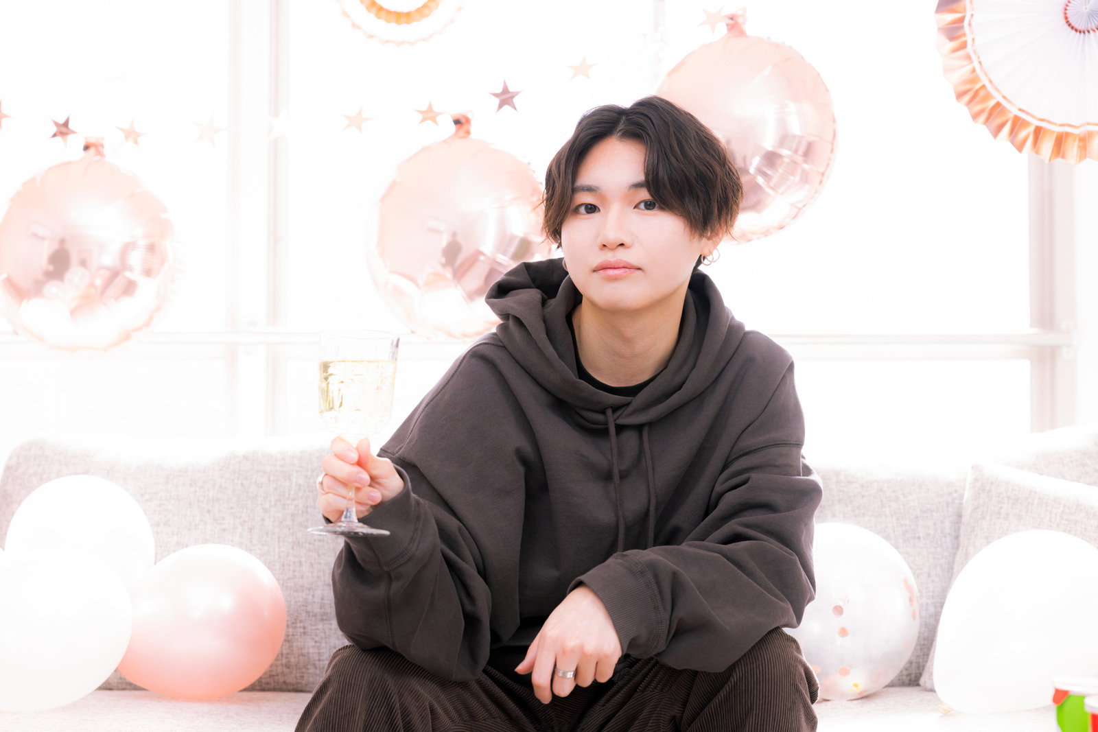 グレーのパーカーを着た男性がシャンパングラスを持って微笑んでいる［モデル：SHUN］