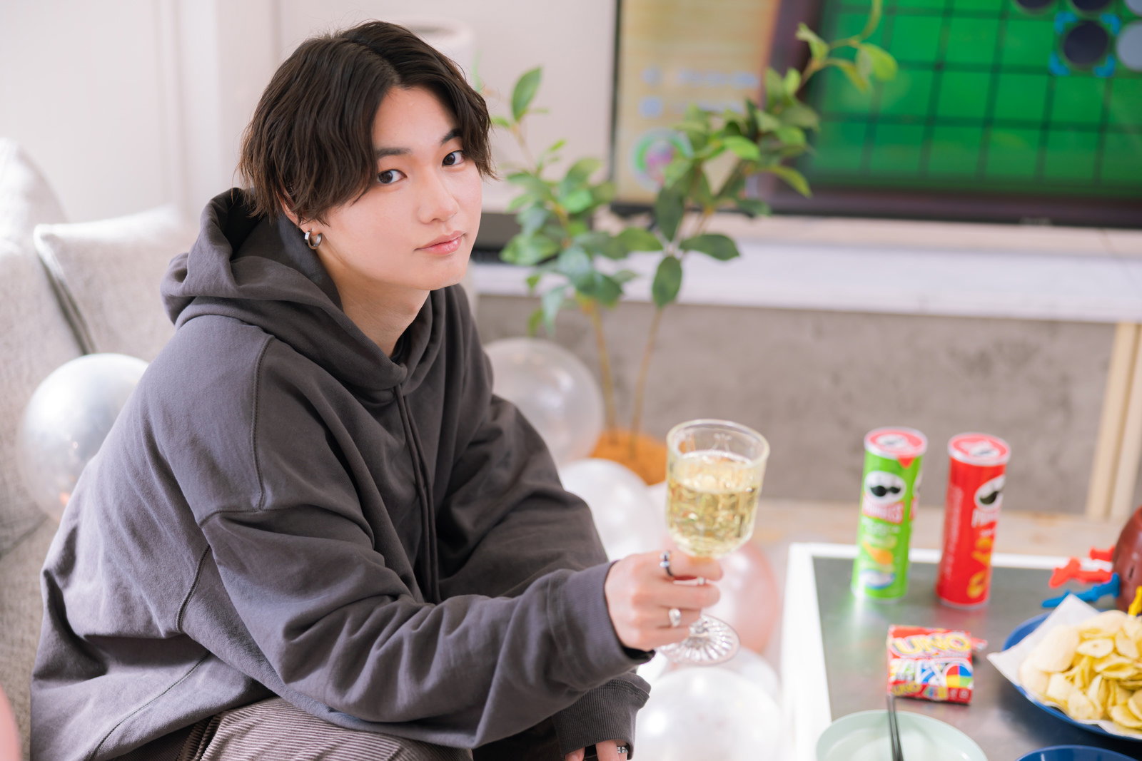 グレーのパーカーを着た男性がテーブルに座りホームパーティを楽しんでいる［モデル：SHUN］