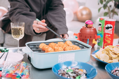 ホットプレートを囲んでタコパしてる様子、友人たちの楽しい食事風景