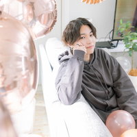 ソファーに座ってこちらを見つめるグレーシャツの男性の写真