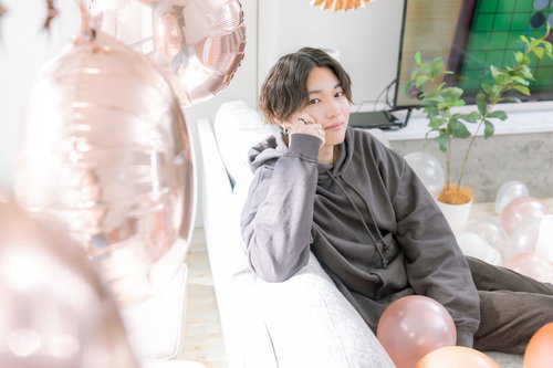 ソファーに座ってこちらを見つめるグレーシャツの男性