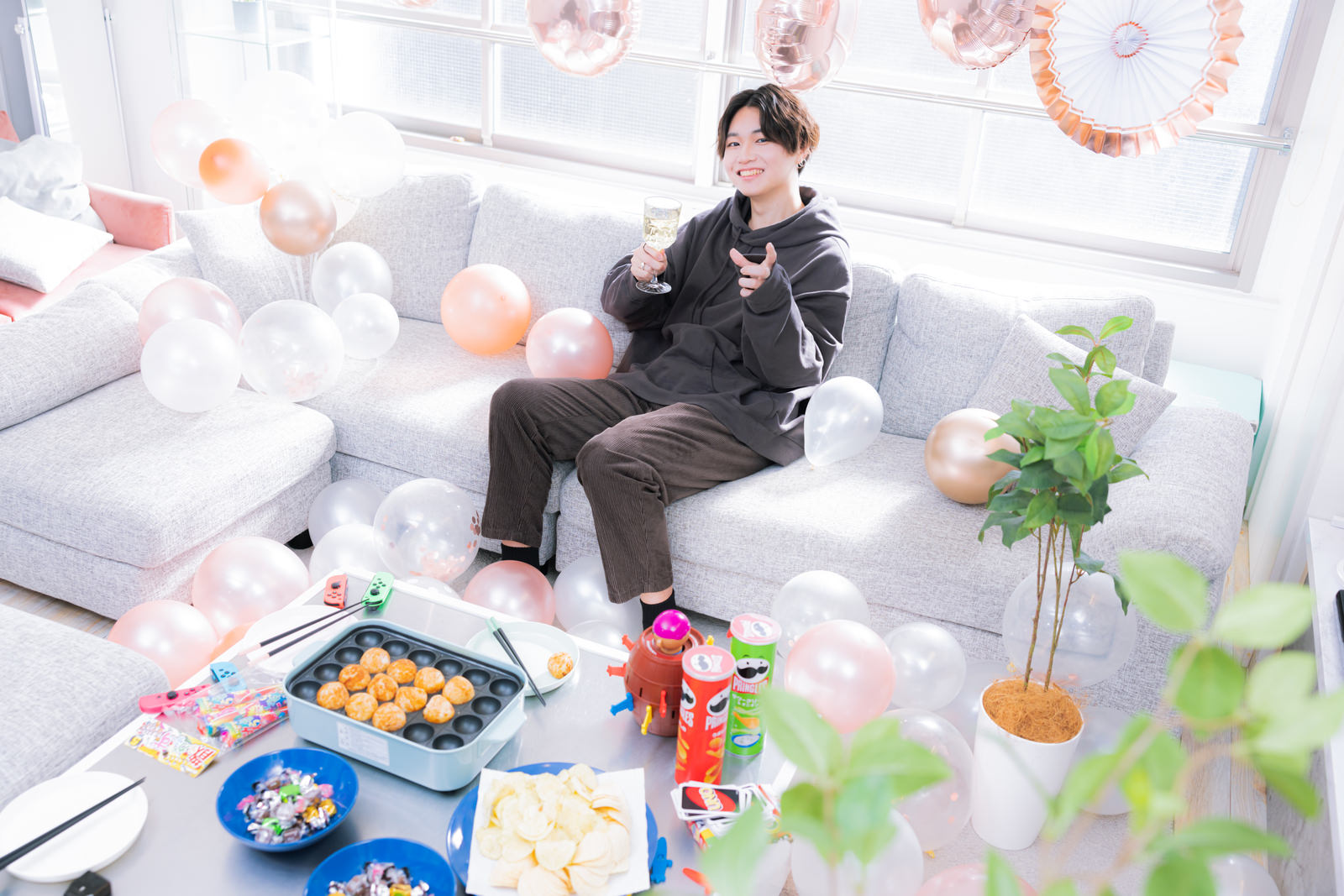 ソファに座りシャンパンやお菓子を楽しむ女性のホームパーティー風景［モデル：SHUN］