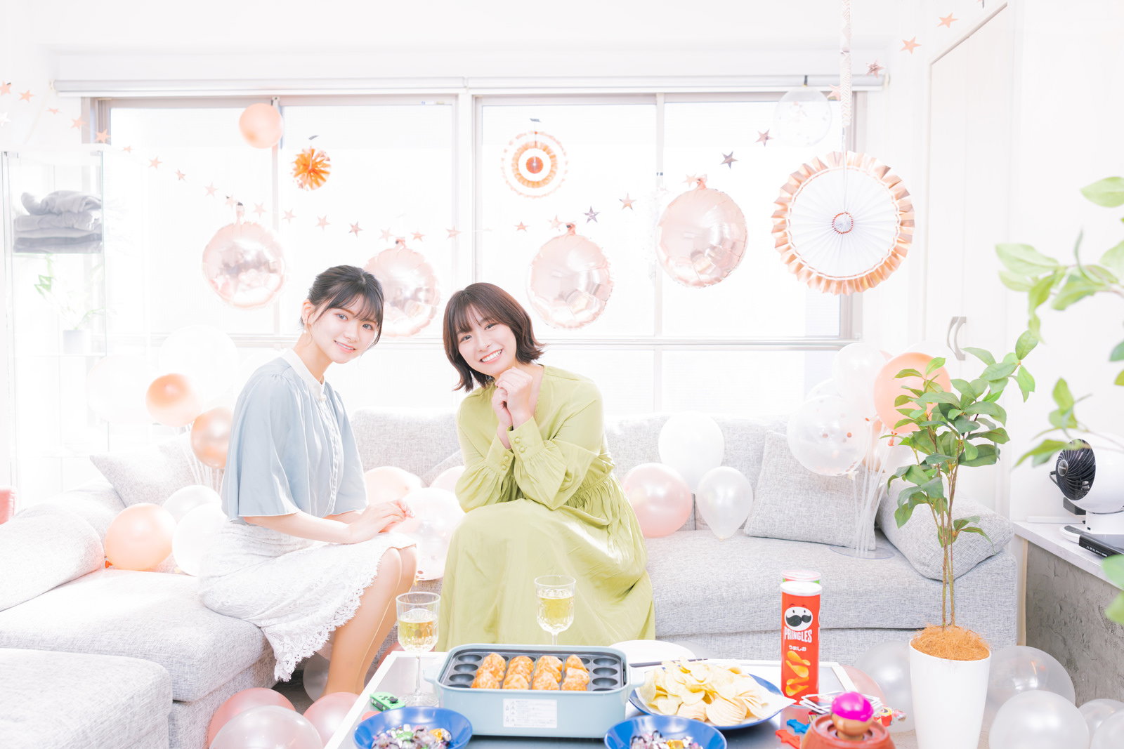 明るいリビングのソファでくつろぐ緑のワンピースと白いシャツの女性二人［モデル：モデルリリース 夏実］