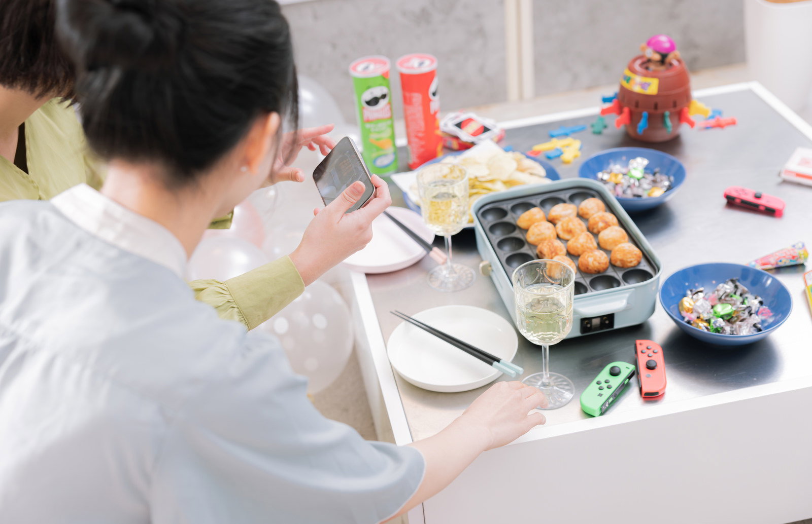 テーブルのたこ焼きパーティーをスマートフォンで撮影している女性［モデル：モデルリリース 夏実］