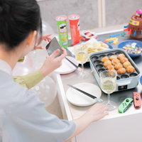 たこ焼きパーティーをスマートフォンで撮影する女性の写真