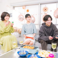 ホームパーティーで家庭用ゲームを対戦プレイする男女三人の写真