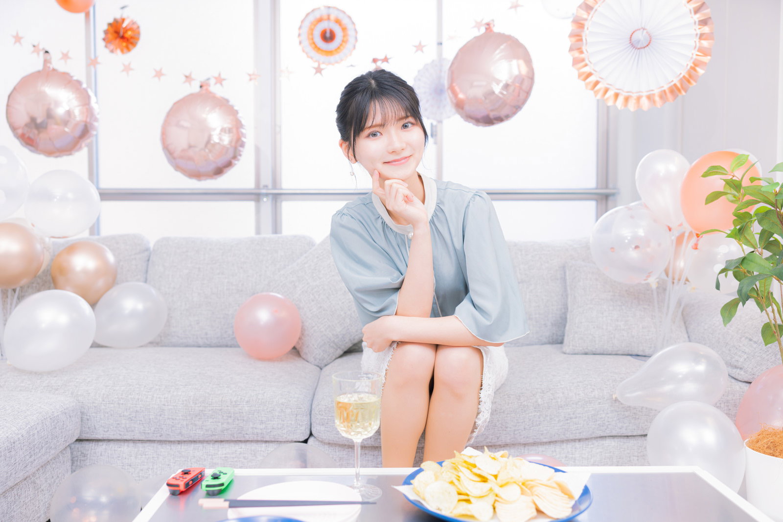 ピンクの風船やパーティー装飾が飾られた部屋でソファに座る女性［モデル：モデルリリース］