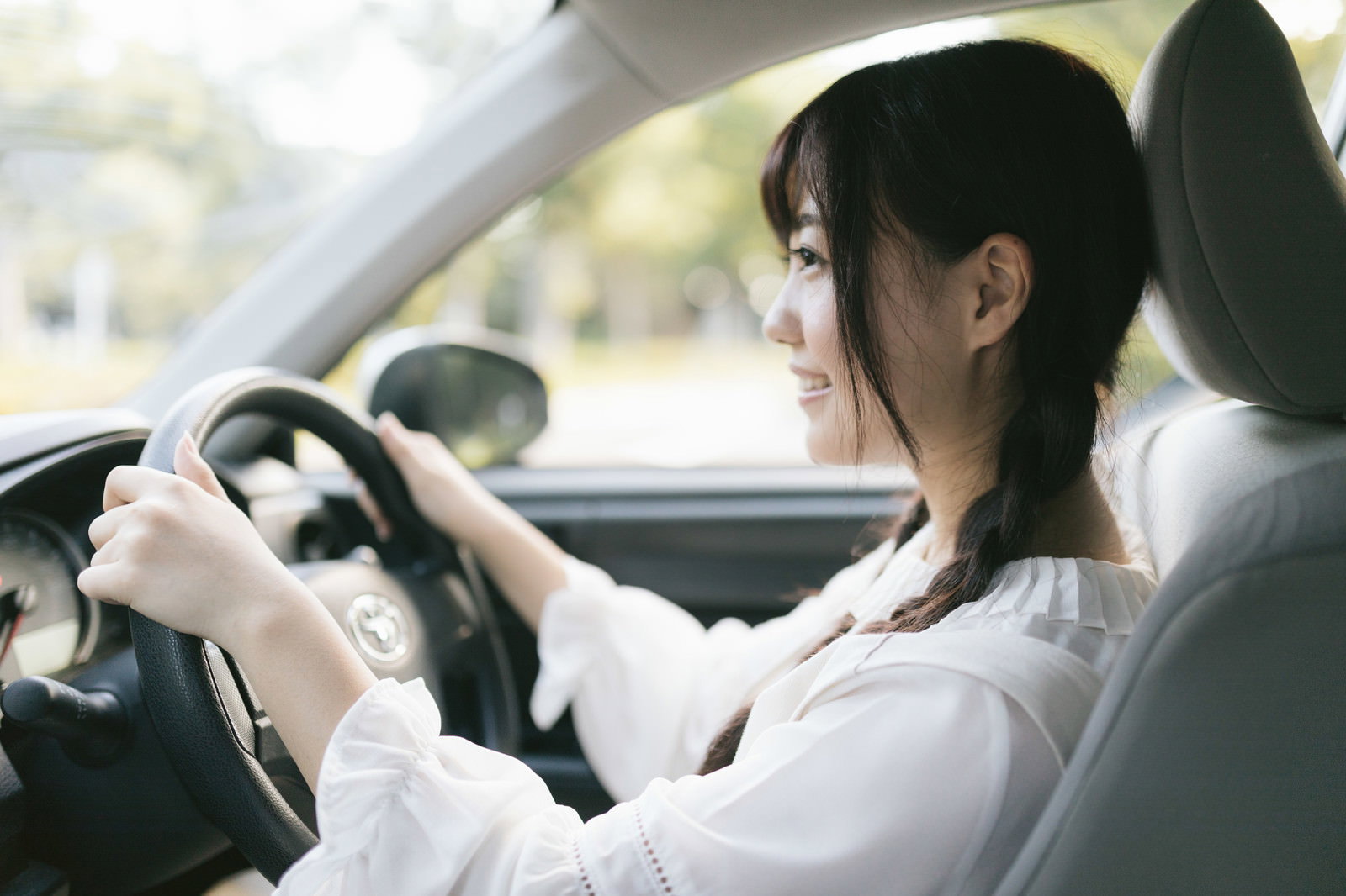 車内でハンドルを握り前方を見つめる白いシャツの女性ドライバー［モデル：河村友歌］