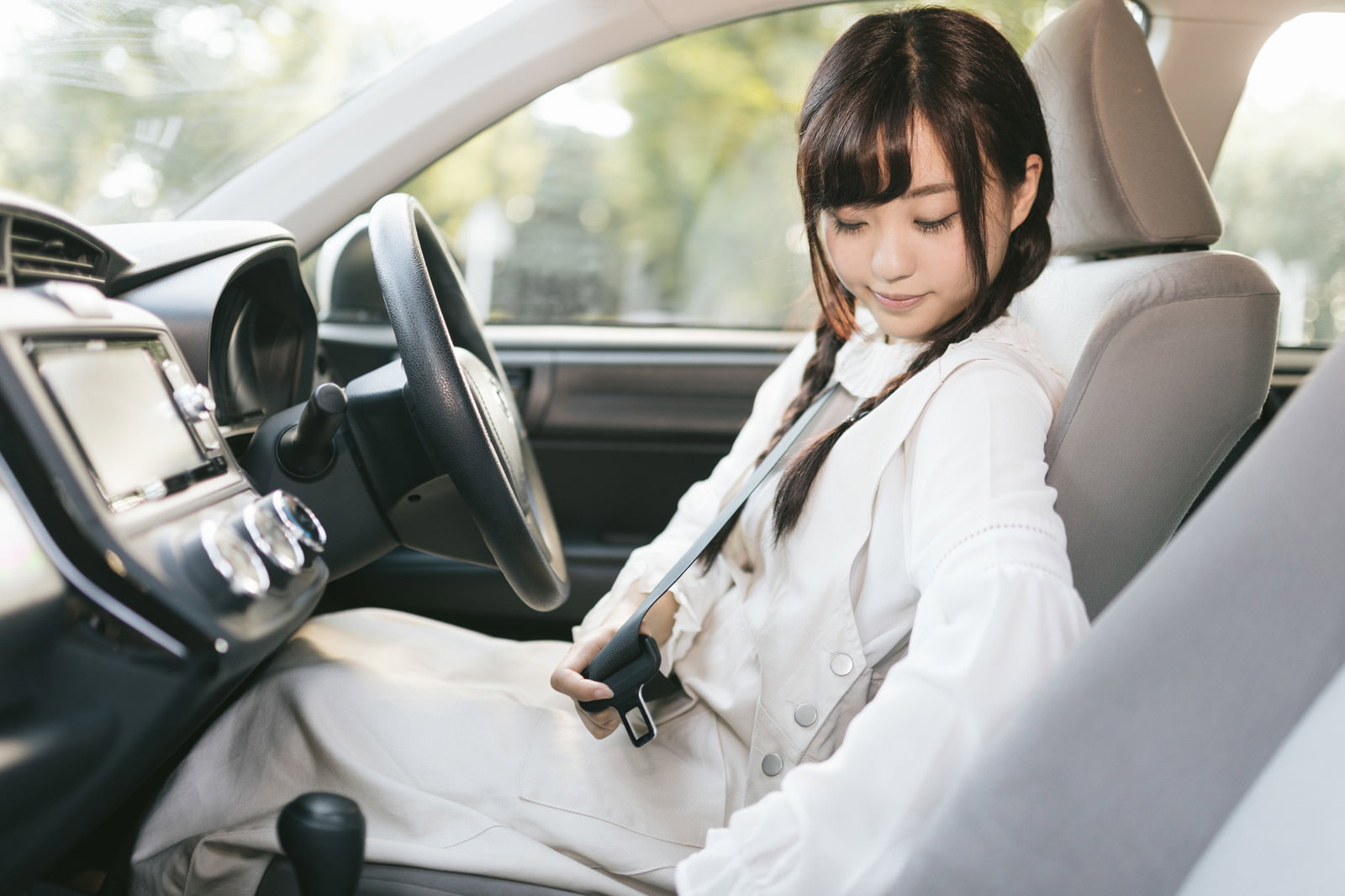 車の運転席でシートベルトを装着する白いシャツの女性［モデル：河村友歌］