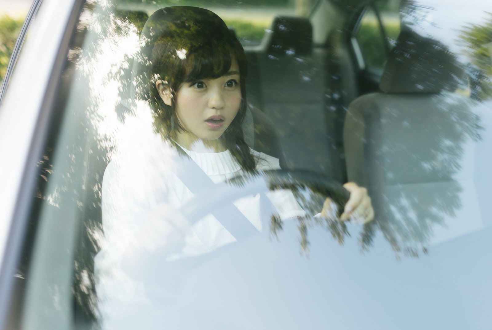 車内で急ブレーキをかけながらハンドルを握る女性ドライバー［モデル：河村友歌］