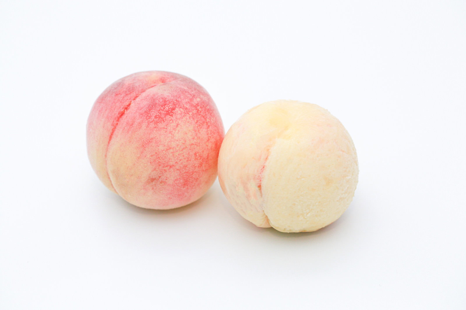 白い背景に皮を剥いた桃と剥く前の桃が2個並んで置かれている