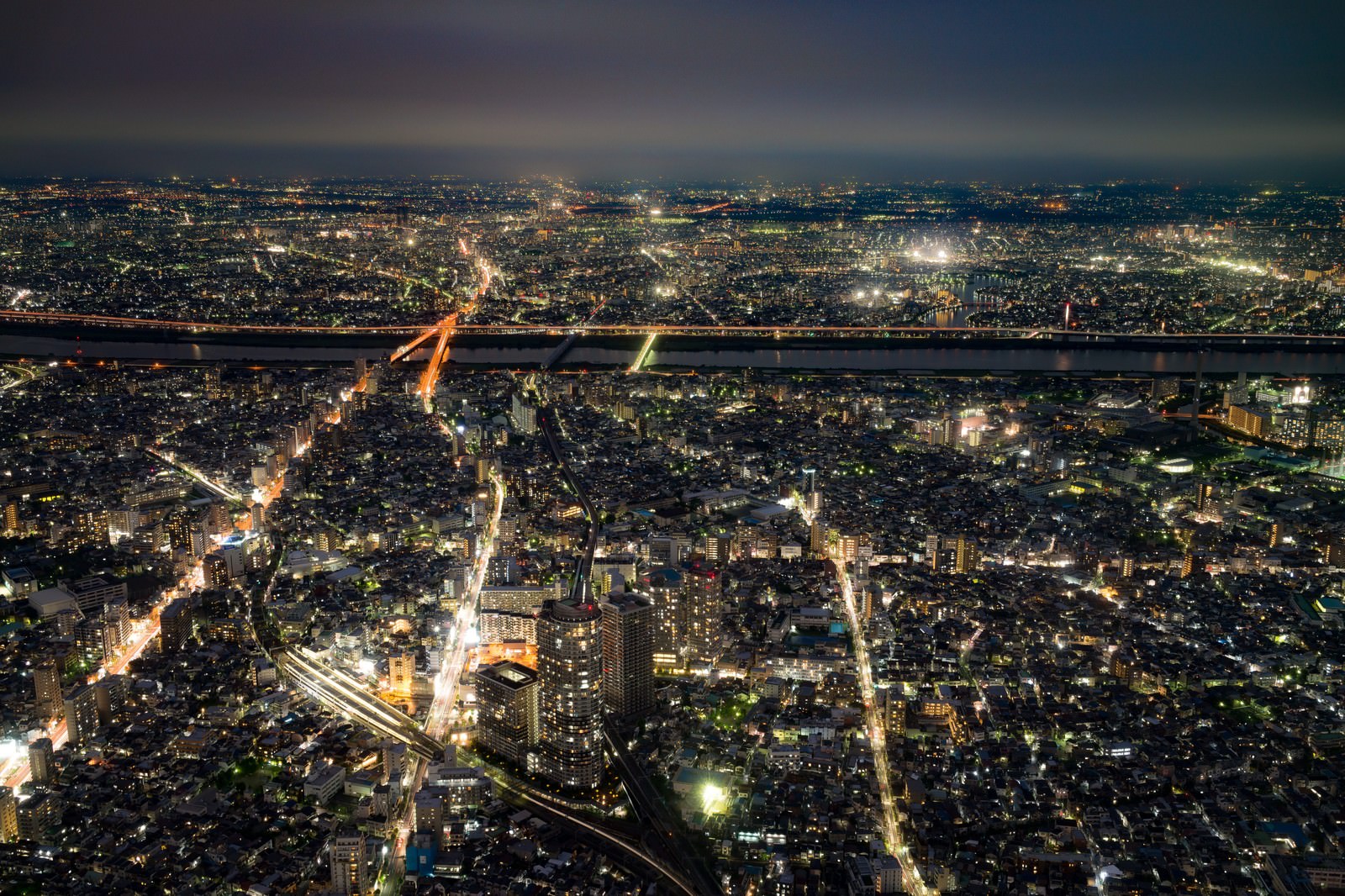 河を挟んで広がる夜間の街並み。建物が密集し、橋が照らされている。