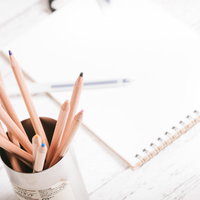 白い背景に配置した木製の鉛筆立てとノートの写真