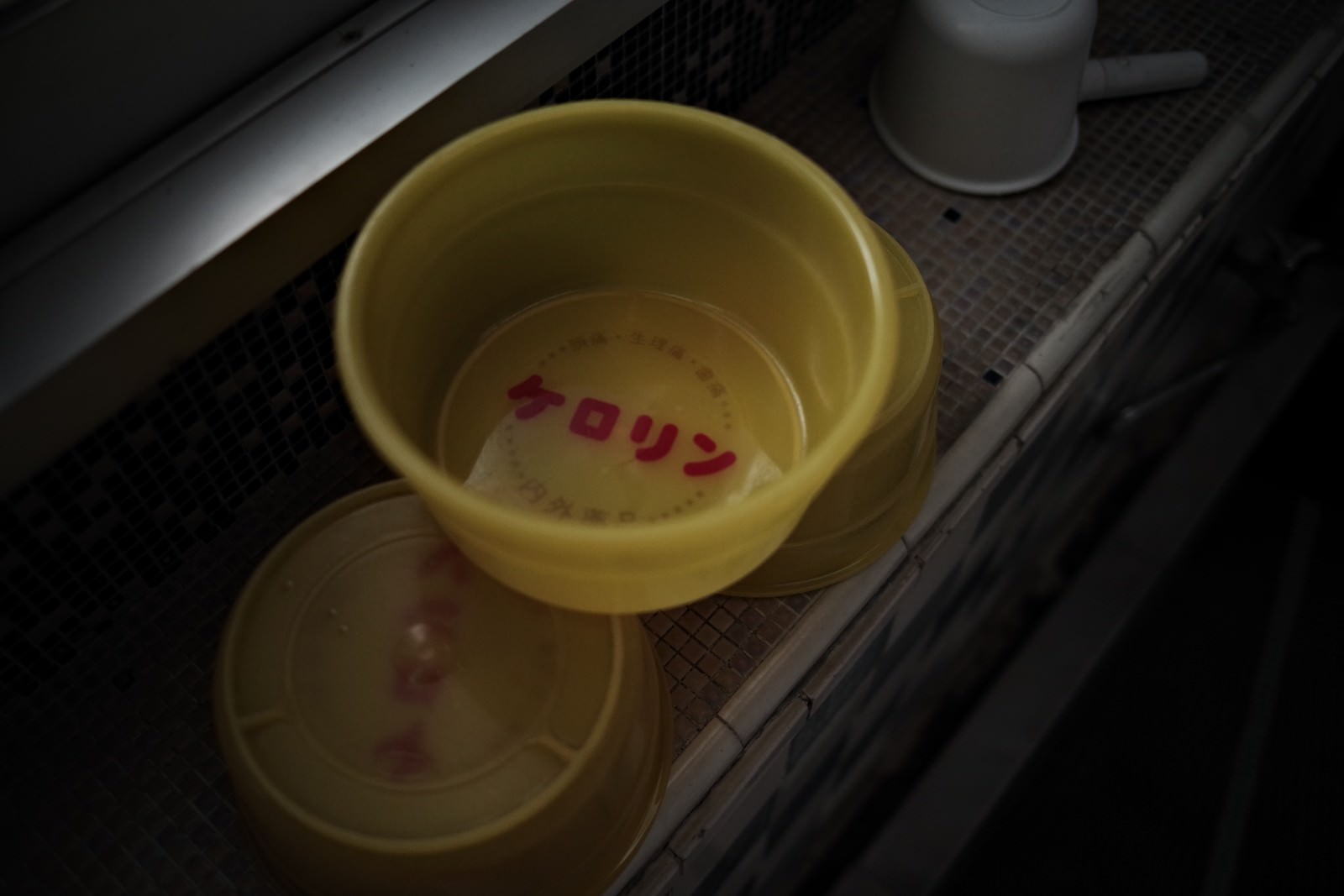 A yellow Kerorin bathtub bucket placed on the edge of the bathtub in a dimly lit public bath