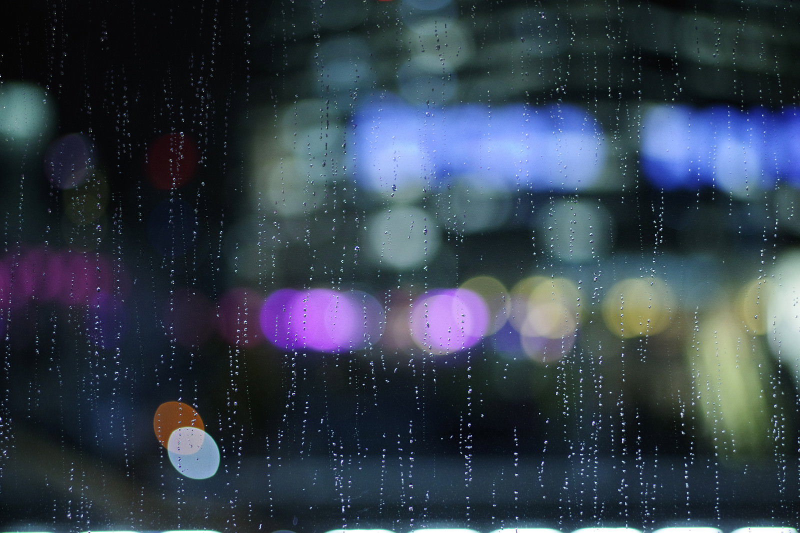 雨に濡れたガラス越しに見える色とりどりのネオンの光がボケて映る様子