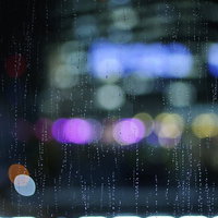 雨に濡れたガラス越しに映るネオン光と水滴の夜景の写真