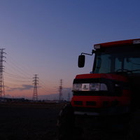 夕暮れ時の送電線とトラクターのシルエットの写真