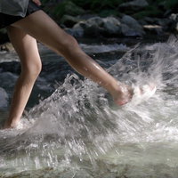 渓流で水遊びする子供の足元と水しぶきの写真