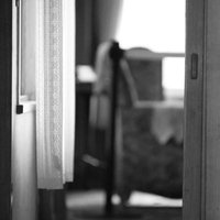 柔らかな光が差し込むモノトーンの部屋の開きかけたドアの写真