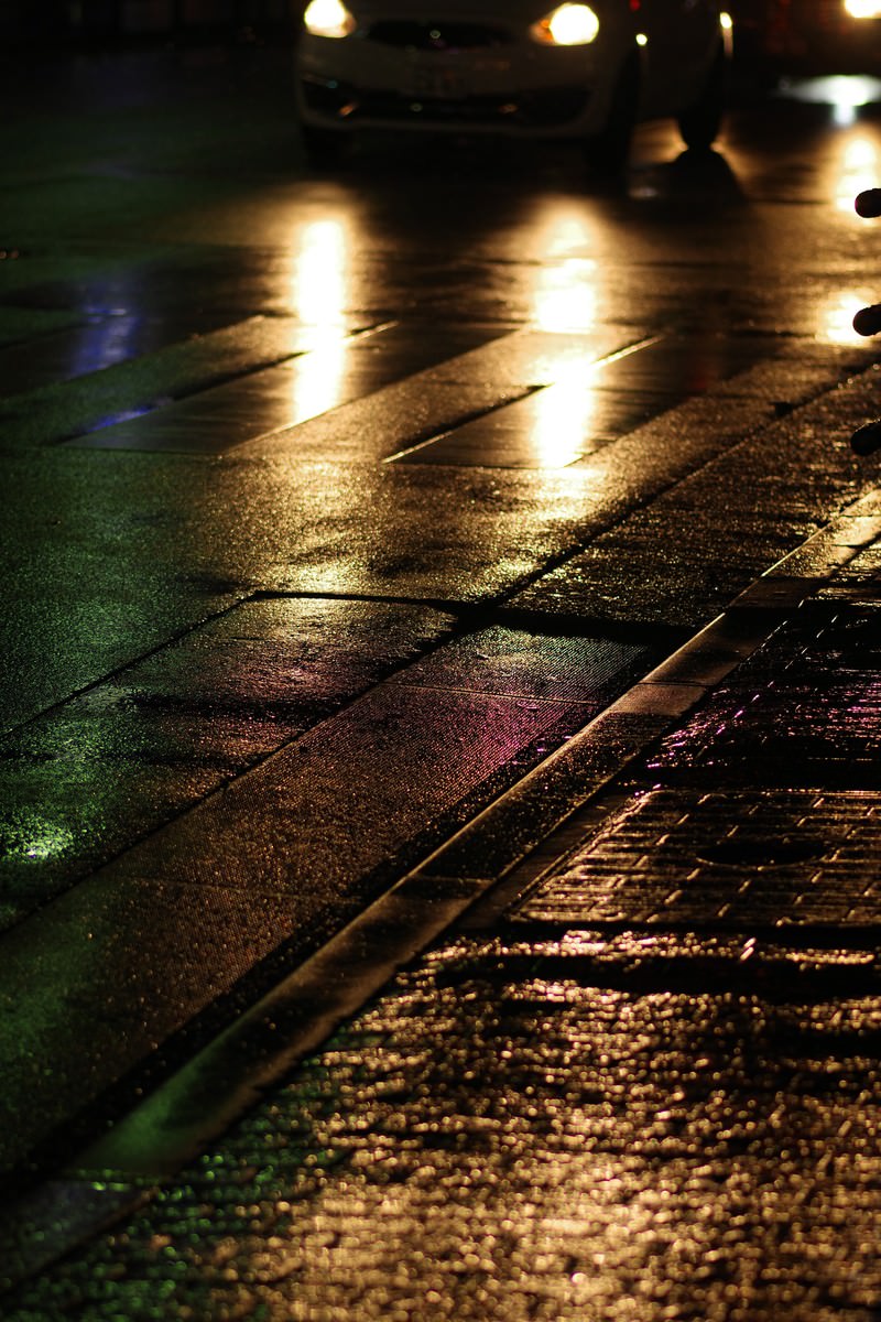 雨に濡れた道路にヘッドライトが反射している夜の横断歩道