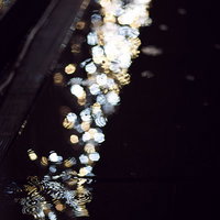 側溝の水たまりに映る街灯の光と雨の夜景の写真