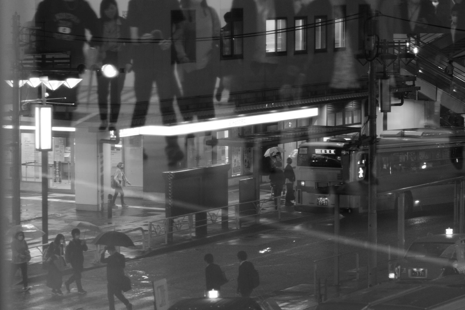 雨の夜、駅前で傘をさして歩く多くの帰宅者たちのモノクロ写真