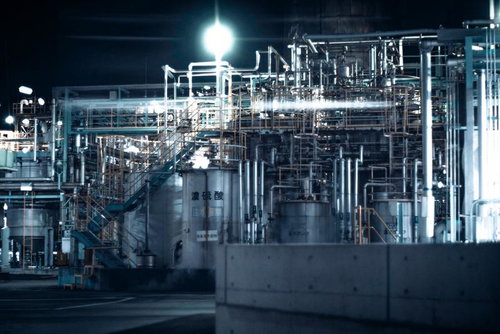 夜間照明に浮かぶ配管とタンクの工場夜景、蒸気立ち上る産業施設