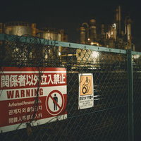 立入禁止のフェンス越しに望む夜間の工場夜景の写真