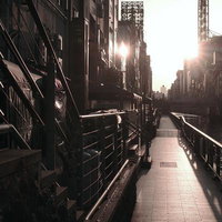 夕陽が沈む都会の川沿いの遊歩道を行く人影の写真