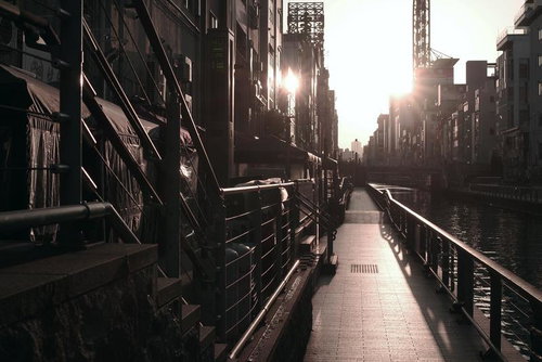 夕陽が沈む都会の川沿いの遊歩道を行く人影