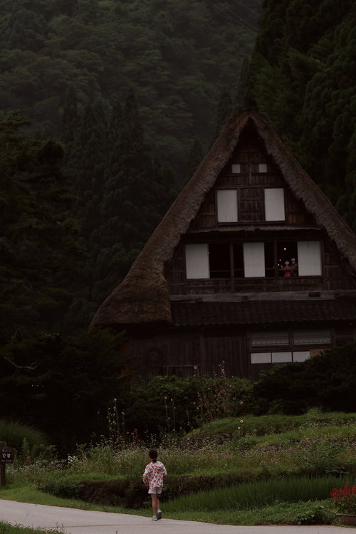 茅葺屋根の合掌造りを背景に相倉集落を散歩する女の子