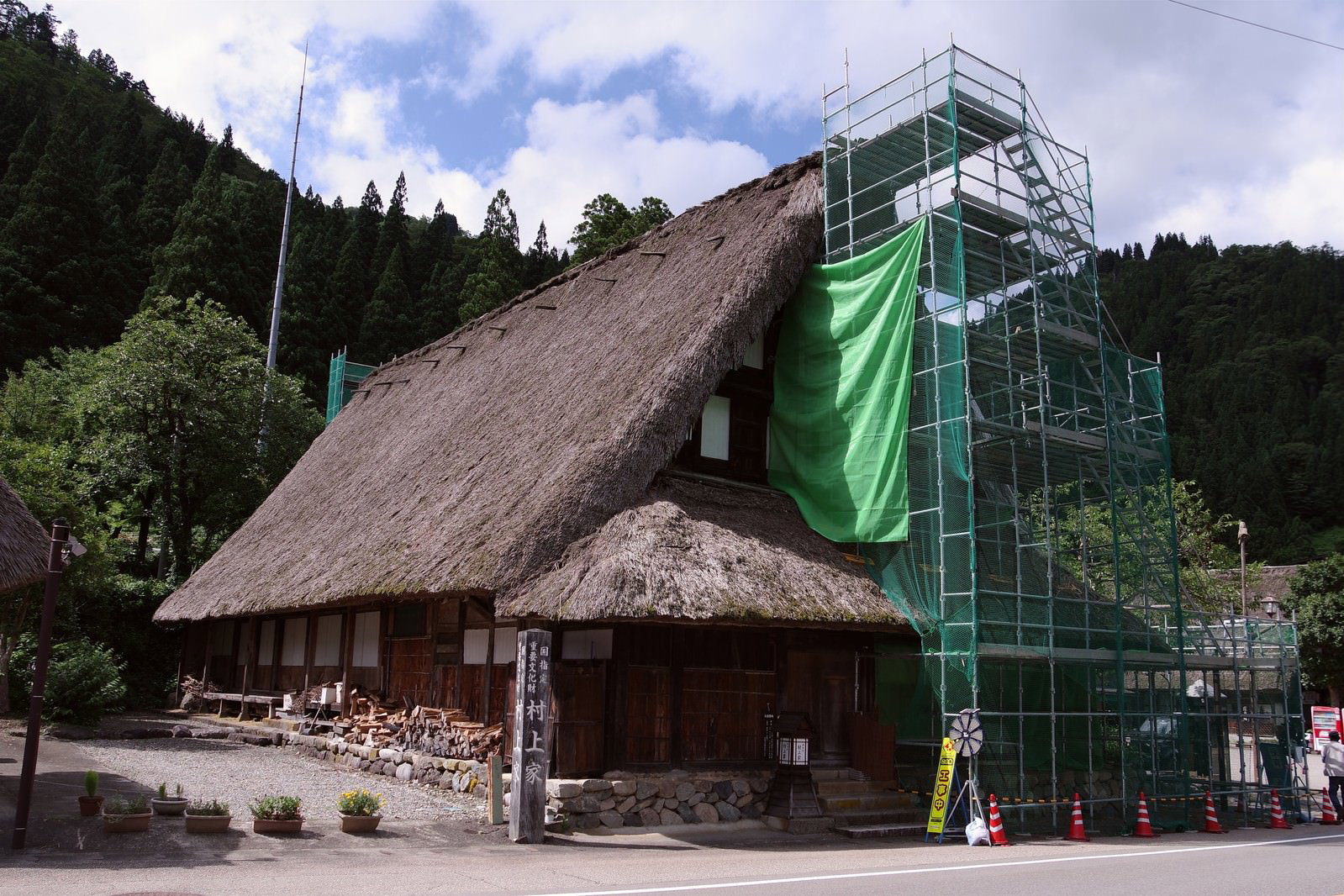 茅葺屋根の合掌造り建物に緑の足場が組まれた葺き替え工事の様子