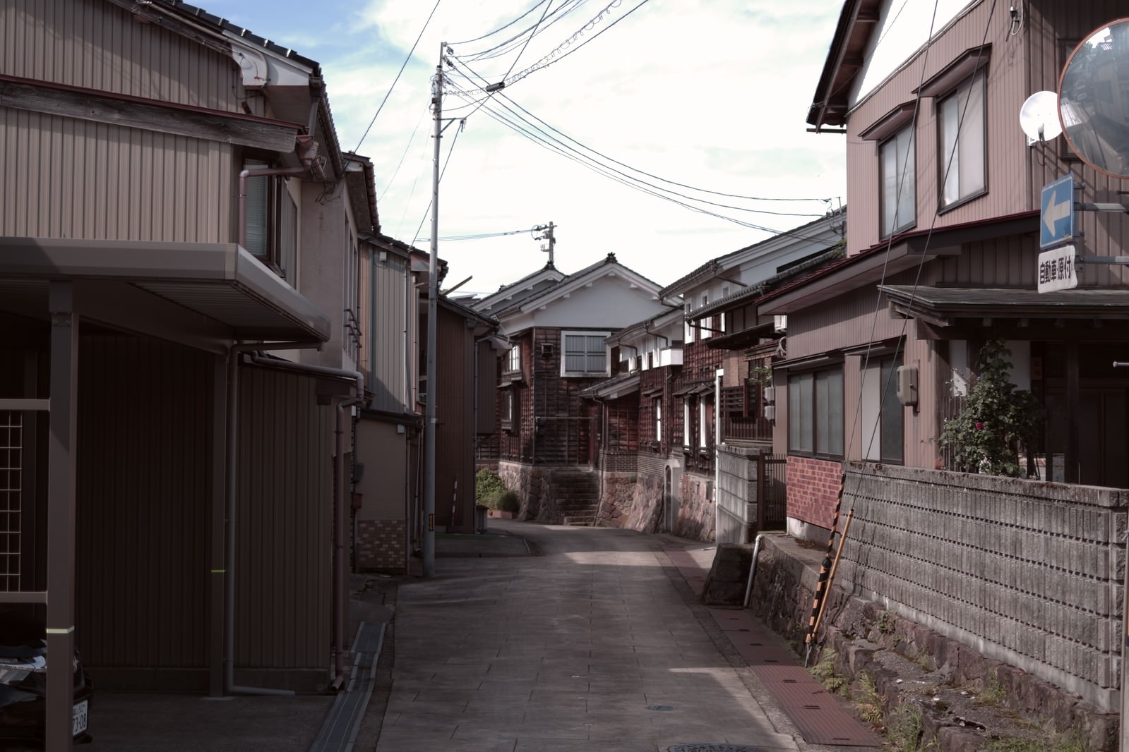 富山県南砺市の住宅街を通る小路。両側に民家が建ち並び電線が見える静かな街並み