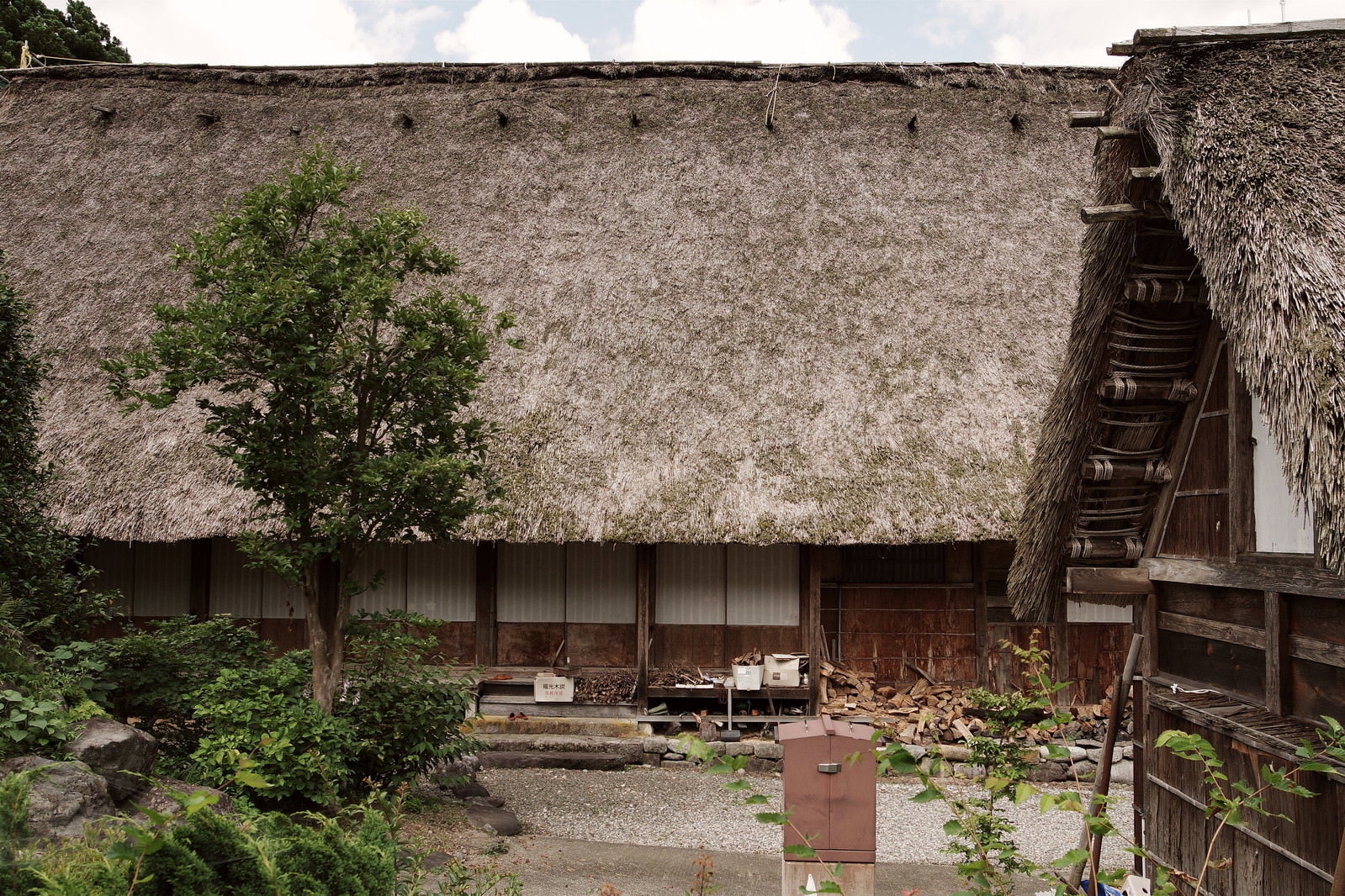 茅葺屋根の民家と軒下に積まれた薪の風景
