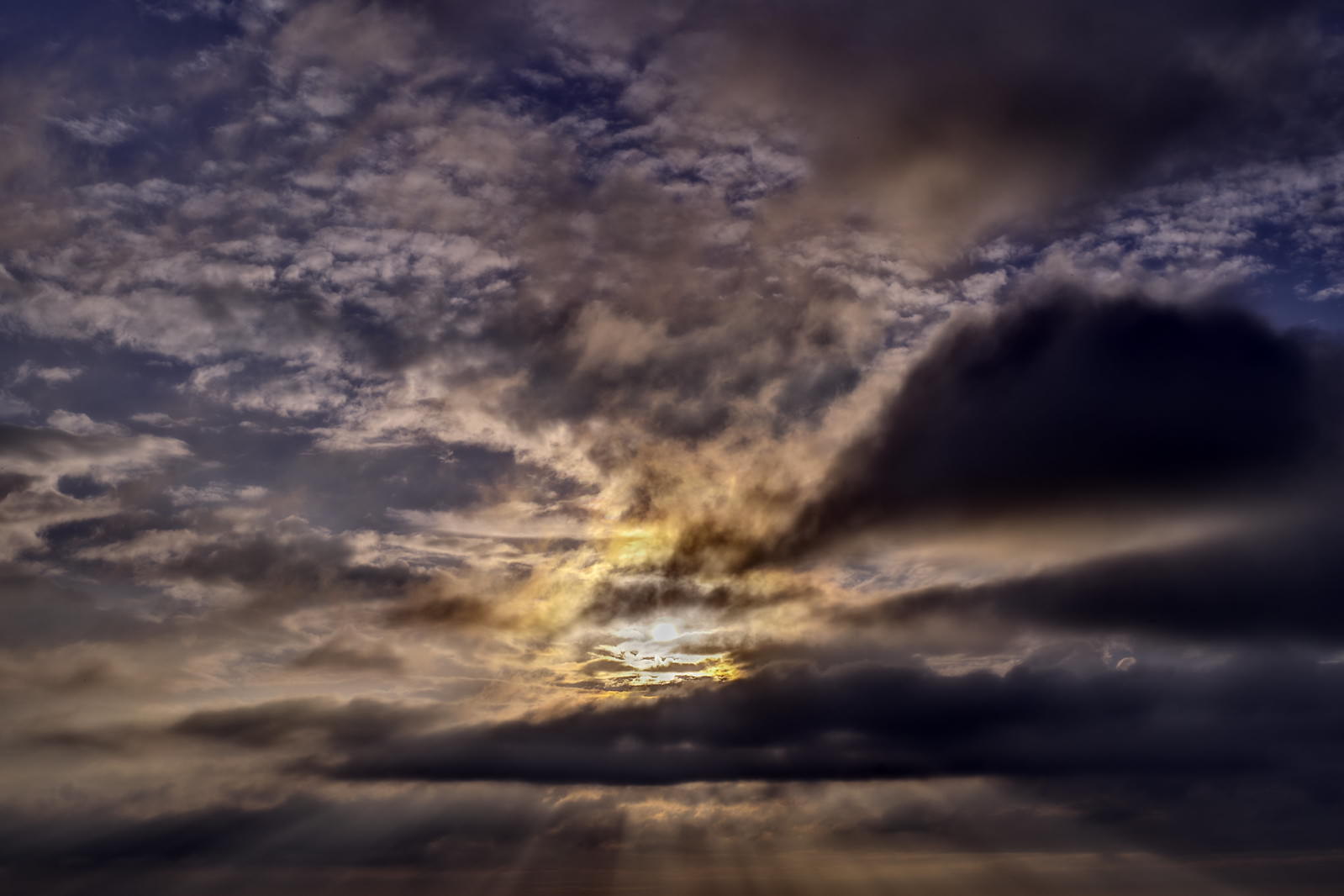 厚い雲の隙間から差し込む薄明光線が美しい夕暮れ空