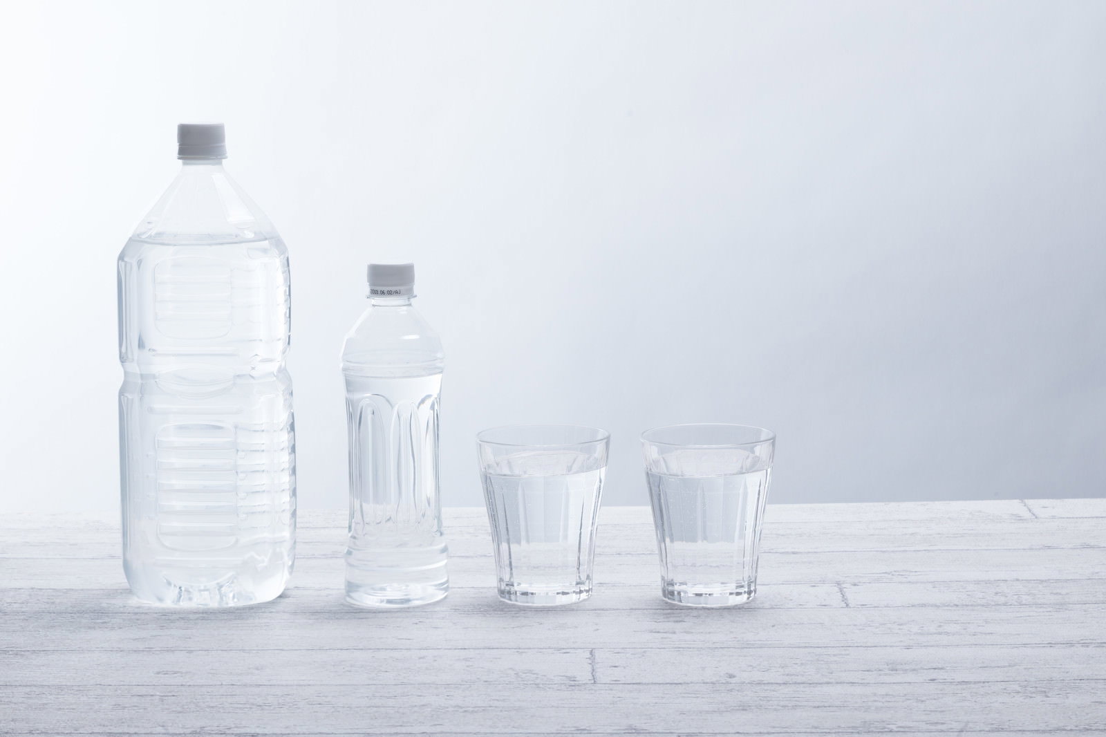 白い背景に透明なペットボトル2本とグラス2個のミネラルウォーター