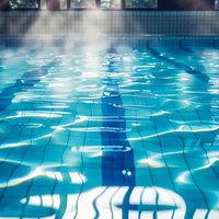 日差しが降り注ぐ施設内プールの水面と青いレーンの写真