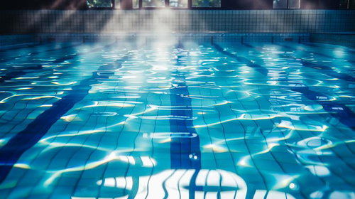 日差しが降り注ぐ施設内プールの水面と青いレーン