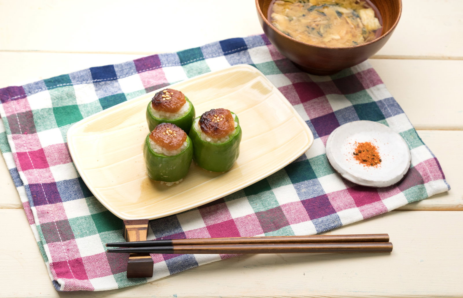チェック柄のランチョンマット上に置かれた、ピーマンに焼きおにぎりを詰めた料理
