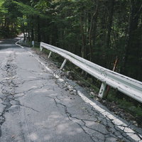ひび割れた山道と傾いたガードレールの写真