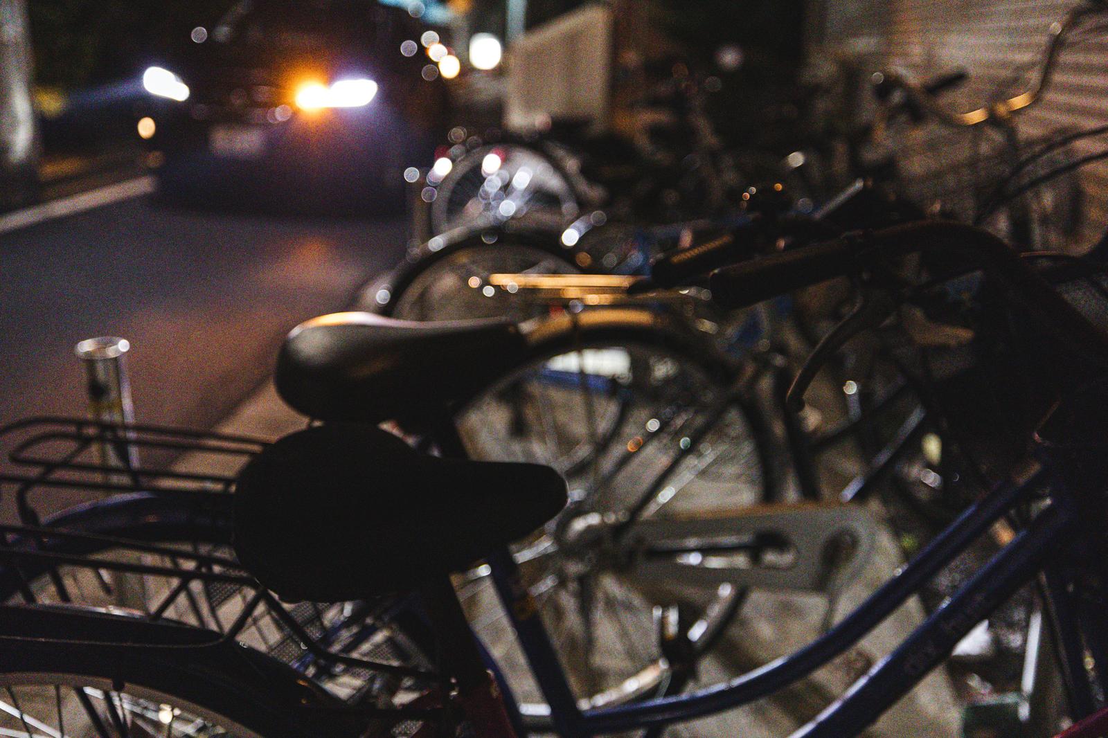 夜間のマンション駐輪場に停まる複数の自転車と背景の通行自動車