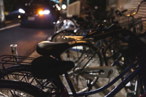 夜間のマンション駐輪場と通る自動車の細い路地