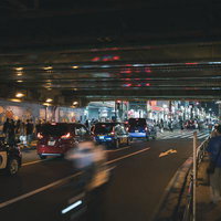新大久保駅高架下の夜間、信号待ちの車と通行人が行き交う駅前風景の写真
