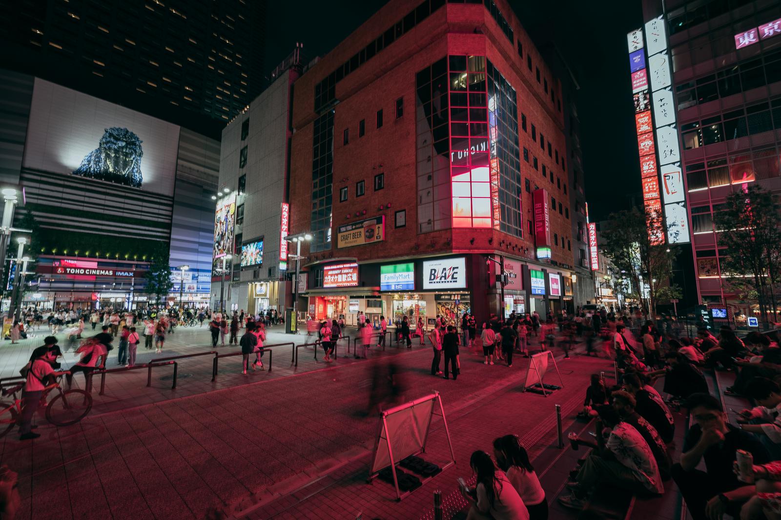 赤いネオン照明に照らされた新宿・歌舞伎町のシネシティ広場に大勢の人が集まる夜景