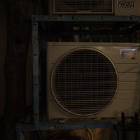 夜間に照らされた暗いエアコン室外機と配管設備の写真