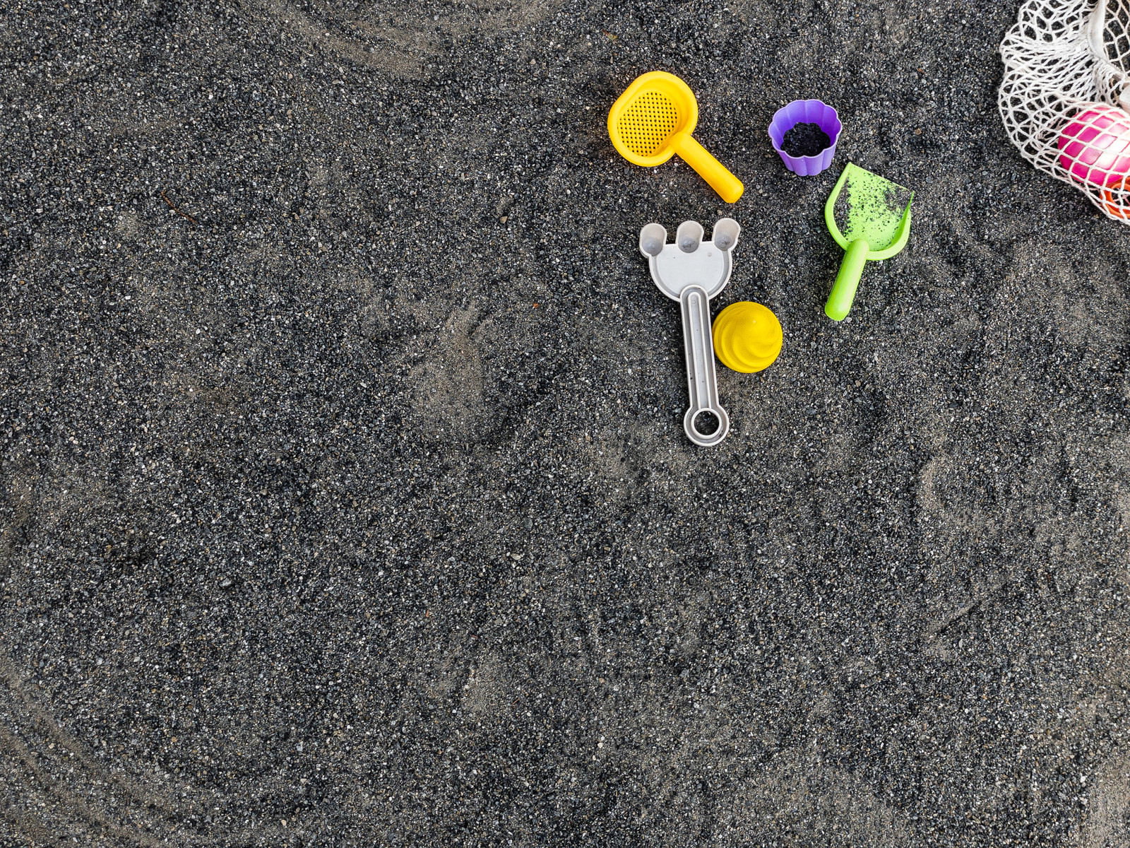砂場に黄色や紫色のバケツとスコップが散らばっている様子