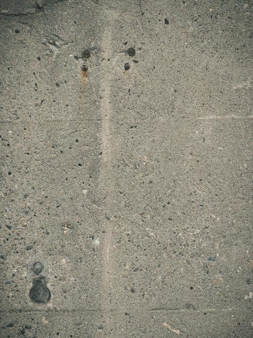 大小の小石が埋まるグレーのコンクリート擁壁のテクスチャー