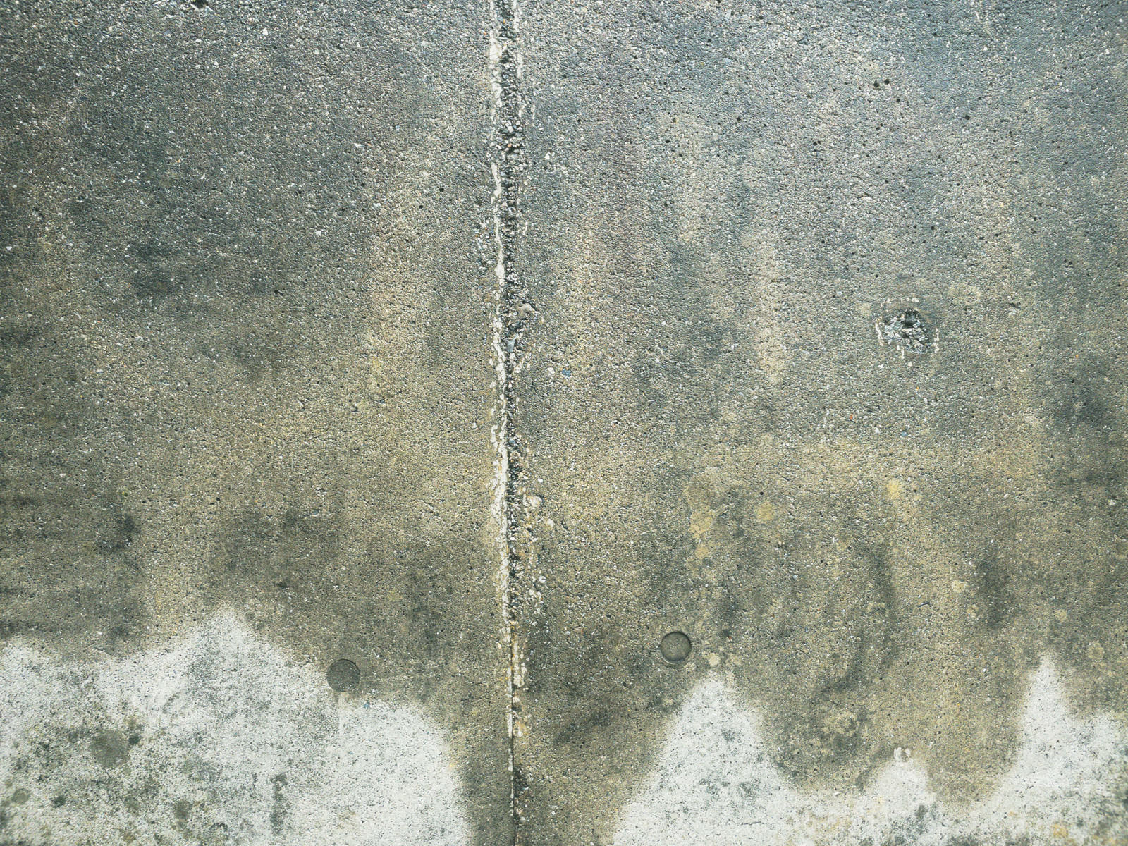 白華が発生し縦にひび割れが入った灰色のコンクリート擁壁